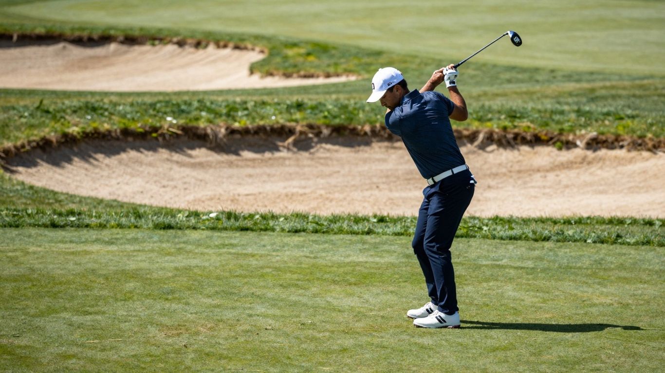 Golfer chips ball near green, sunlight on club.